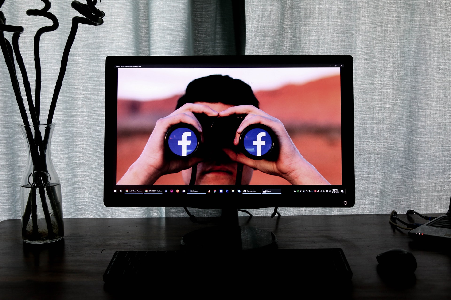 A computer screen in a dark room. The screen shows a man looking through binoculars. The binocular lens' have the facebook logo photoshopped in.